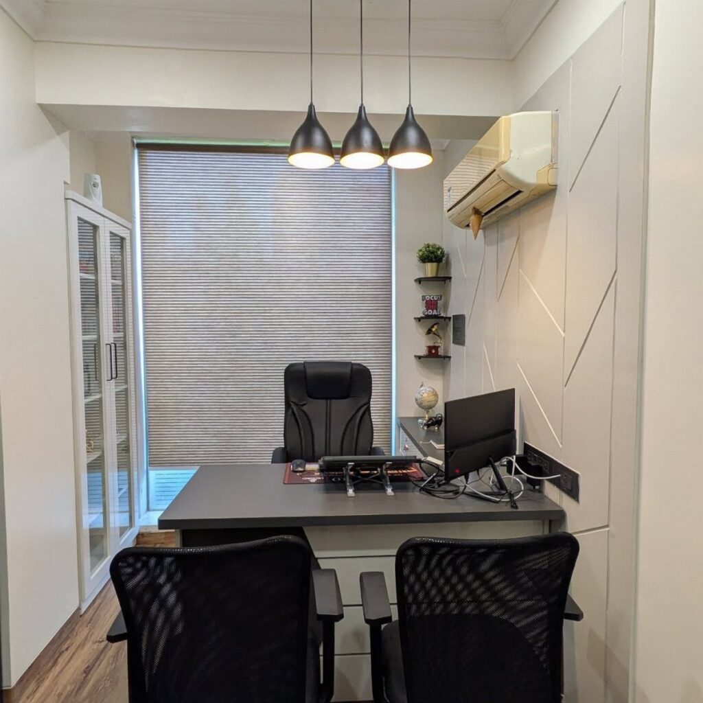 Modern small office with grey desk, black chairs, and three black pendant lights.