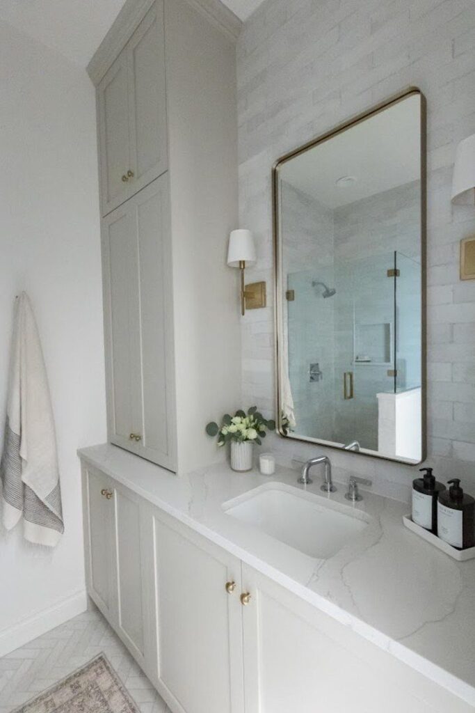 White bathroom vanity with chrome faucet and gold-framed mirror reflecting a chrome shower