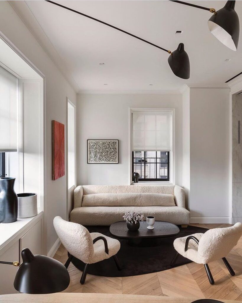 Modern living room with cream bouclé furniture, black accents, and herringbone wood floors.