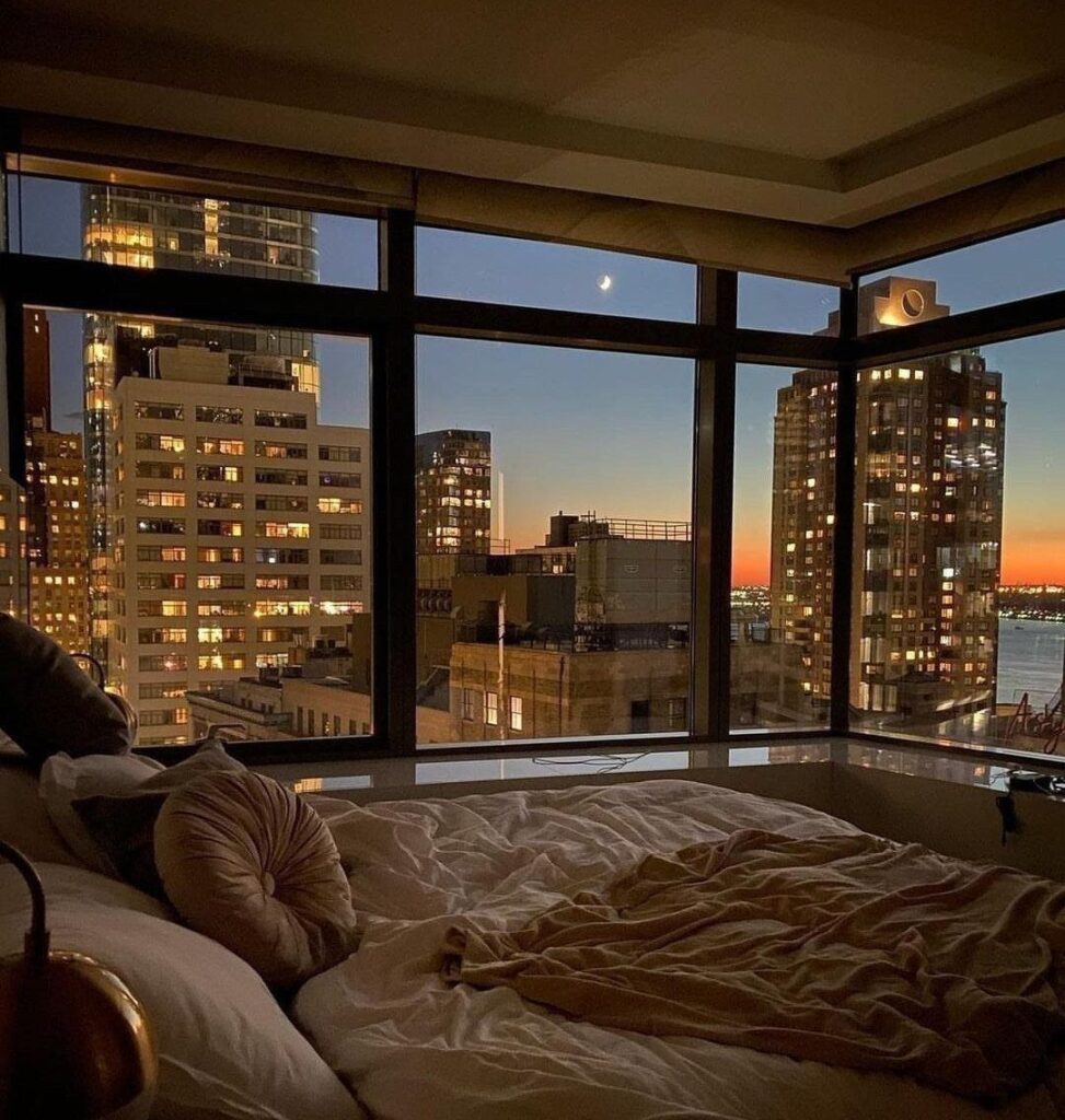 City skyline view from a bedroom window during a golden hour sunset.
