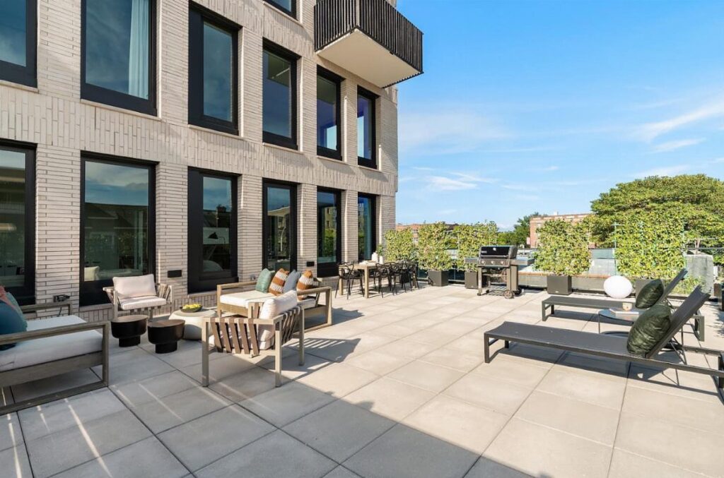 Modern apartment terrace with lounge furniture, dining area, and potted plants under blue sky