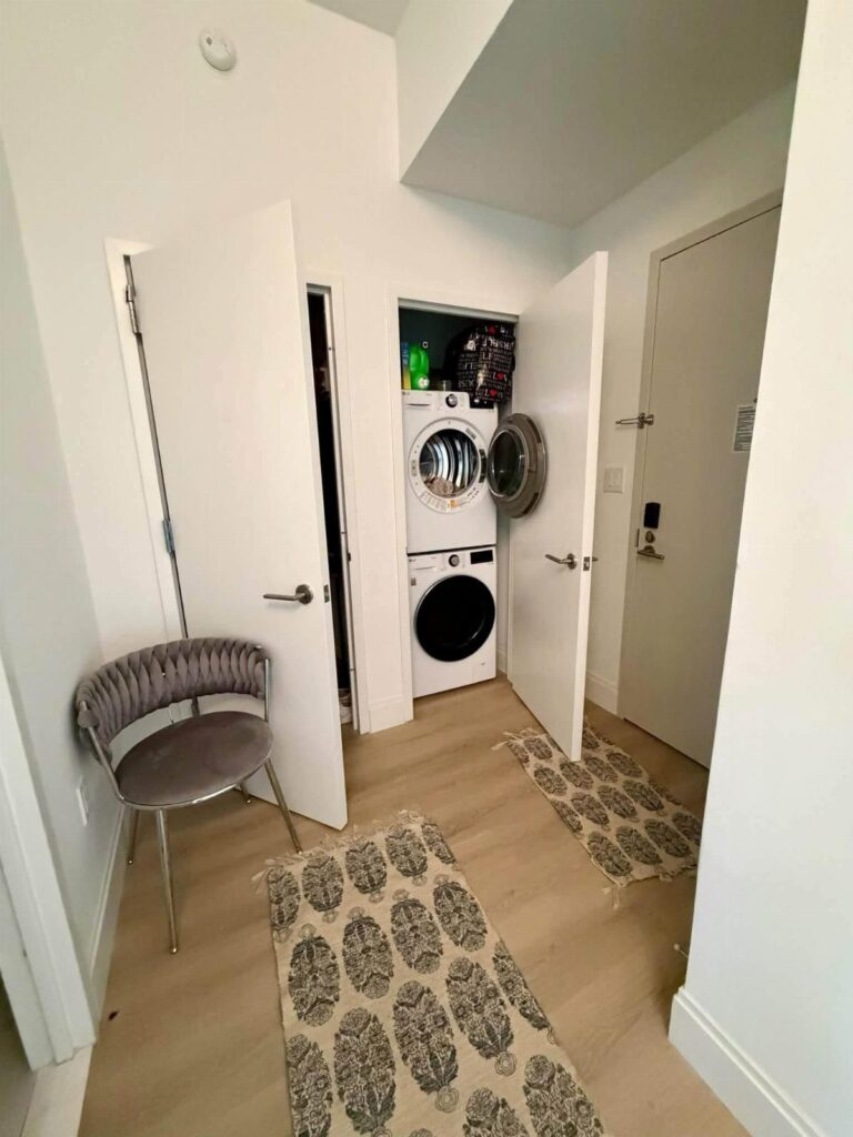 Narrow apartment hallway featuring a stacked washer and dryer in a small alcove.