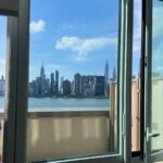Manhattan skyline and river viewed through an open apartment window under blue sky