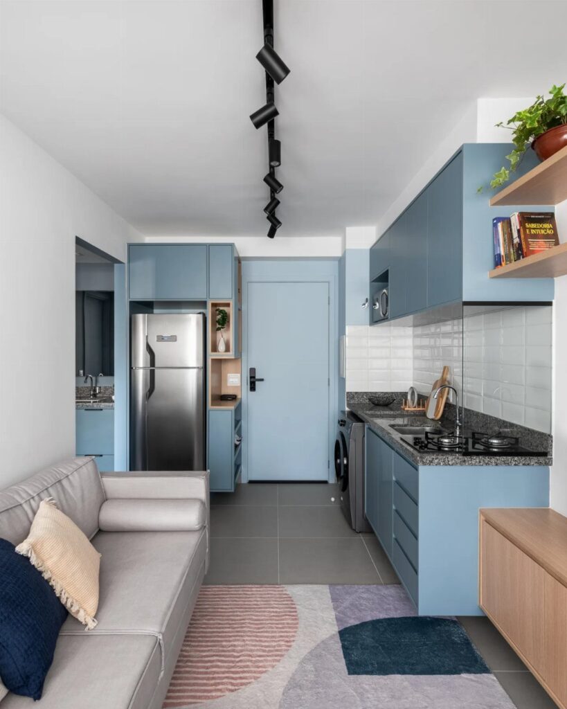Studio apartment interior with blue kitchen cabinets, grey sofa, and colorful area rug.