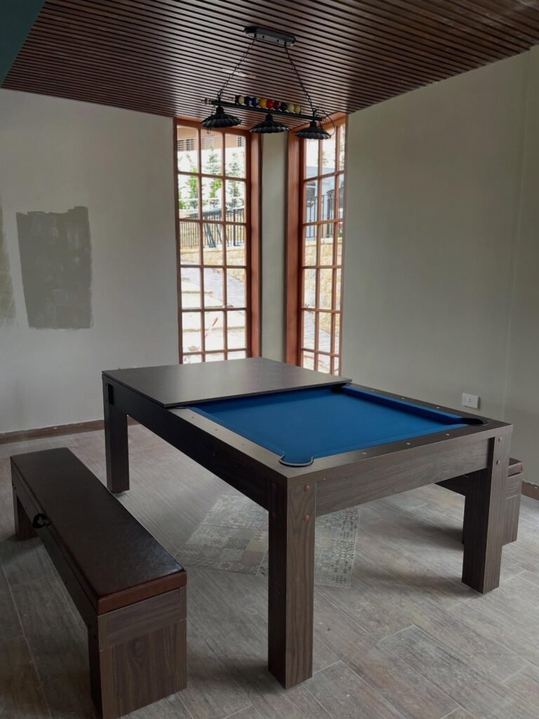 Blue felt pool table with wooden cover and bench in a small room