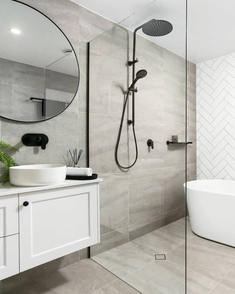 Modern small bathroom featuring a white freestanding bathtub, grey tiles, and black fixtures.