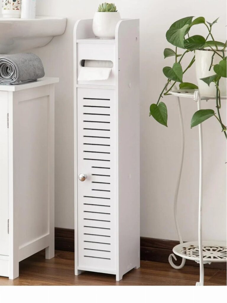 Slim white bathroom storage cabinet with a slatted door and small potted plant.