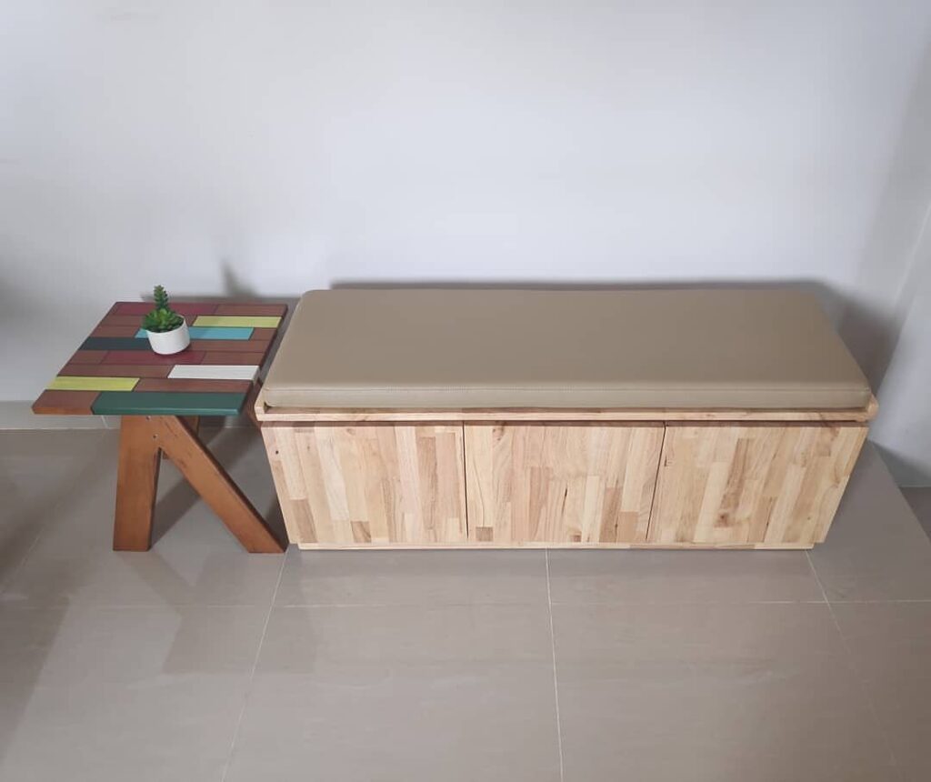 Wooden storage bench with beige cushion and a colorful small side table.