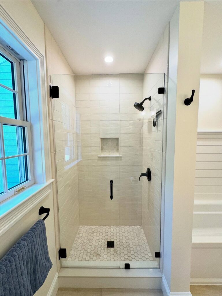 Small walk-in shower with white subway tiles and clear glass door with black hardware.