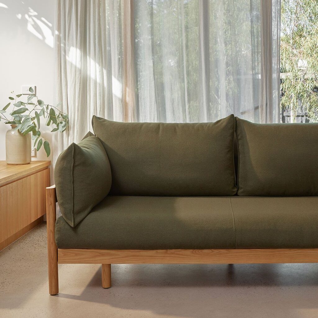Olive green fabric sofa with a light wood frame in a bright room.
