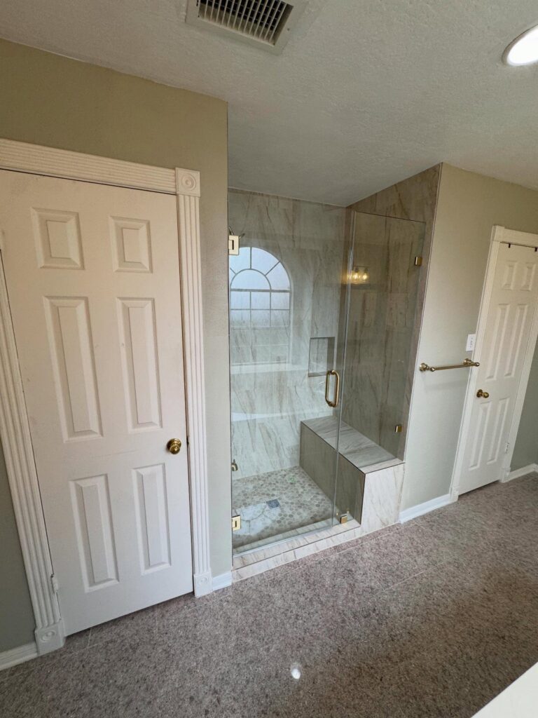 Walk-in shower with glass enclosure and marble bench in a neutral room