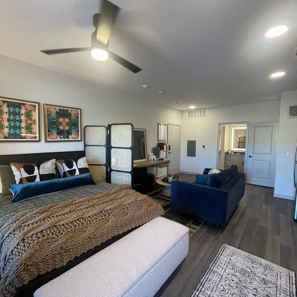 Studio apartment interior with a bed, blue sofa, and room divider screen.