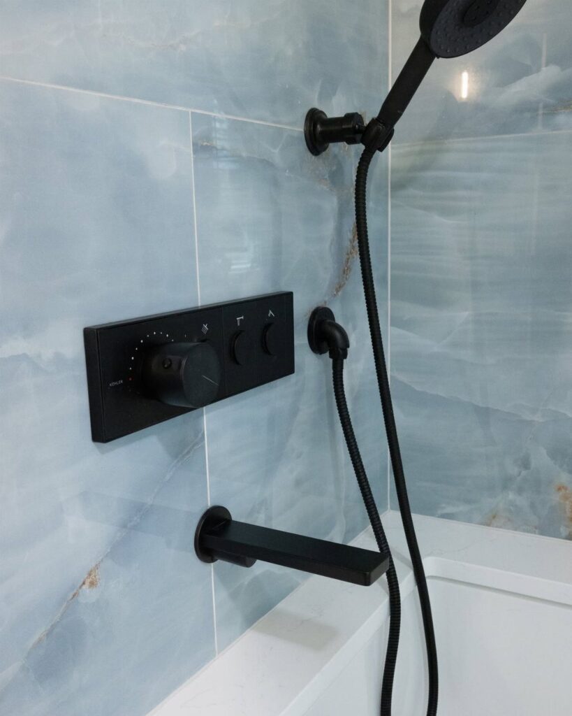 Light blue marbled bathroom tiles with black shower fixtures and a white bathtub.